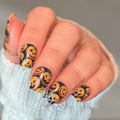 Close-up of manicured nails featuring the Cobweb Creepers design: orange jack-o-lantern pumpkins and black nails with white spiderweb details, displayed on a white knit sweater
