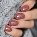 Rose gold glitter nail wraps with a deep rosy shimmer and glossy finish, shown on short natural nails against a soft grey knit background.