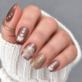 Hand wearing Cozy Cup nail wraps with cocoa-brown shimmer, cream hearts, a snowflake design and a gold glitter accent nail.