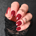 Hand with burgundy nail strips wearing a black textured glove on a dark background