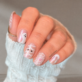 Cute & Creepy nail wraps on hand—clear iridescent base with white and pink spiderwebs, ghost, and mummy wrap designs
