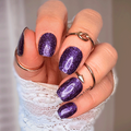 A close-up image of a person's hand with fingernails painted in a glittery deep blue nail wraps and royal purple colour, with the person wearing a lace glove and several rings on the fingers.
