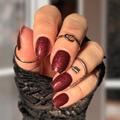 Hand with dark red glittery nail wraps wearing black fingerless gloves against a blurred background