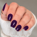 Dark purple glossy nail wraps worn on hand with gold ring against grey background