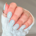 Hand wearing soft blue-green nail wraps with a glossy finish and subtle silvery undertone.
