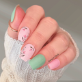 Hand with pastel floral nail design nail wraps wearing a white knit sleeve.