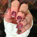 Hand with floral nail wrap design wearing a white textured sleeve against a blurred background