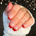 Hand with red nail polish wearing a white sleeve against a dark background with confetti.