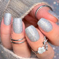Close-up of hands with glittery silver nail strips and multiple rings.