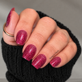 Close-up of dark pink glitter nail wraps with gradient cuticle fade on manicured nails, styled with black knit sleeve and gold ring