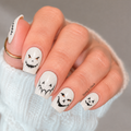 Lantern Lurkers glow-in-the-dark nail wraps applied on nails, showing white base with black jack-o-lantern faces on cream skin tone