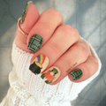 Nail wraps on a hand with festive designs, including a rainbow, pot of gold, and leprechaun.