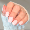 Opaque light pink nail wraps on a hand wearing a soft blue sweater, showing a clean blush pink manicure with a glossy finish.