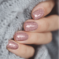 A close-up of a person's fingernails with light pink glitter nail wraps, holding a textured grey fabric.