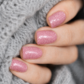 Pink glitter nail wraps on short rounded nails, shown in a close-up manicure against soft grey knitted fabric.