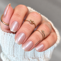Lost Pearl nail wraps with a sheer nude base and pearlescent shimmer on square nails, styled with gold rings and a white sweater.