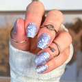 Hand with glittery blue nail polish strips wearing a white sleeve indoors.