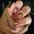 Hand with glittery nail polish strips and gold rings against a dark background