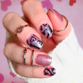 Hand with pink glittery nails and black heart designs on a pink heart patterned background