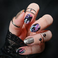Hand with colorful nail art and multiple rings on a dark background