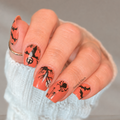 Halloween nail wraps on nails with orange base and black bat and spider designs