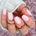Close-up of glossy pale pink Hanny & Chuck nail wraps on a hand wearing gold rings and a white knit sweater.