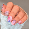 Pink Halloween nail wraps with pastel pumpkins, cute ghosts and spooky black line art on a manicured hand.