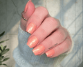 Hand with peach glittery nails against a neutral background