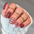 Hand wearing Peppermint Cocoa Christmas nail wraps with burgundy glitter, reddish-brown solids, pale pink stripes and white snowflakes.