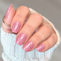 Pink glitter nail wraps on short rounded nails, shown in a close-up manicure against soft white sweater