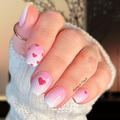 Hand with pink nail polish strips featuring heart designs, wearing a white textured sleeve.