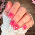 Hand with pink nail polish stickers and heart and now designs, wearing a white sleeve, against a blurred floral background.