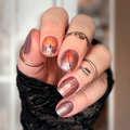 Hand with decorative autumn themed nail wraps wearing a black textured sleeve.