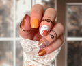 Hand with intricately designed pumpkin and plaid nail wraps in front of a window