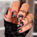 Hand with black nail polish wraps and floral pumpkins designs, wearing a black wristlet.