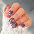 Purple glitter nail wraps with white speckled confetti design on short natural nails, glossy finish with scattered sparkle.
