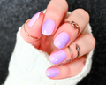 A close-up image of a person's hand showcasing purple and pink ombre nail wraps in varying shades of lilac.