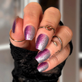 Hand with purple and silver glittery nail polish wraps wearing a black sleeve.