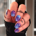 Hand with purple galaxy nail design nail wraps wearing black fingerless gloves against a blurred background