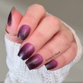 Hand with purple gradient nail wraps wearing a white sleeve.