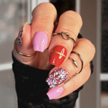 Close-up of a hand with colorful red and fink floral nail art and multiple rings against a blurred background