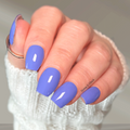 Hand wearing glossy creamy periwinkle blue nail wraps with lavender undertones and a soft pastel finish.