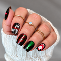 Black Christmas nail wraps with Santa, white reindeer, and red and green metallic Christmas trees on a hand wearing a black sweater.