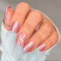Close-up of hand wearing Shimmer & Silk pearl pink marble nail wraps with swirled white and pink patterns, paired with a gold ring and white sweater