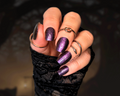 Hand with shimmery purple nail wraps wearing black lace glove against a dark background