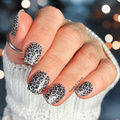 Hand wearing Silver Growl glitter leopard nail wraps with silver sparkle and black spots against blurred bokeh background