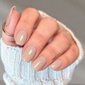Hand wearing glossy nude beige Sip & Snuggle nail wraps with a white knit sweater.