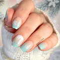 Hand with light aqua and peach gradient nail polish stickers against a blurred background