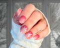 Hand with pink nail wraps and snowflake designs, wearing a light blue sweater.