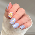 Hand with light blue nail polish featuring spring chicken designs on a neutral background